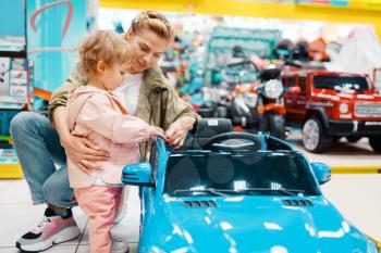 Mother with her little girl choosing electromobile in kids store. Mom and child buying toys in supermarket together, family shopping