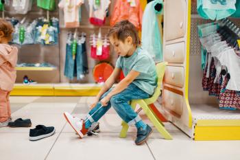Little boy trying on shoes in kids store, side view. Son choosing sneakers in supermarket, family shopping, young customer