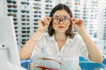 Female buyer tries on many glasses at the same time, optics store, showcase with spectacles on background. Professional eyecare, eyeglasses shop