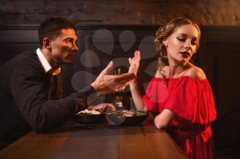 Quarrel of young couple in restaurant, bad relationship. Elegant woman in red dress and her man eating in cafe
