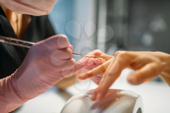 Beautician in pink gloves sticks the nails of female client, manicure in beauty salon. Manicurist doing hands care cosmetic procedure