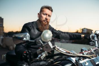 Brutal bearded biker poses on chopper in city, front view. Vintage bike, rider on motorcycle