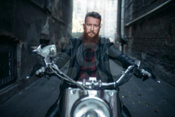 Bearded biker in leather jacket sitting on classical chopper, front view. Vintage bike, rider on motorcycle