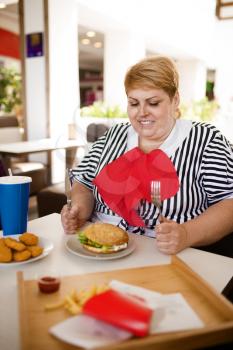 Fat woman prepares to eats fastfood in mall food court. Overweight female person at the table with junk lunch