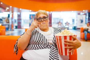 Fatty woman eating popcorn in the cinema hall, unhealthy junk food. Overweight female person in mall, obesity problem