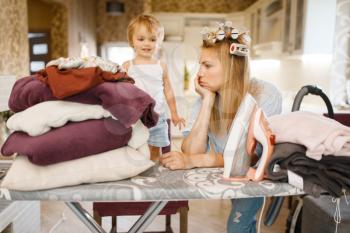 Housewife with little kid at the ironing board. Woman with child doing housework at home together. Female person with daughter in their house