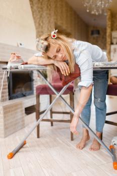 Young tired housewife slepping on the ironing board. Woman doing housework at home. Female person irons the clothes in the house