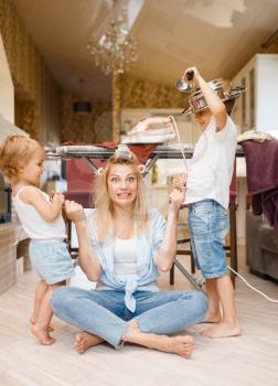 Young housewife with playful kids on the kitchen. Woman with child doing housework at home together. Female person with daughter having fun in their house