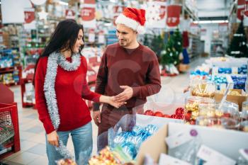 Young couple chooses christmas tree toys in shop, family tradition. December shopping of holiday goods and decorations