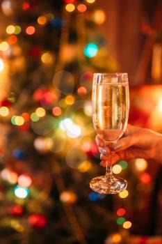 Female hand holds a glass with champagne, christmas tradition, romantic celebration. Xmas symbol to drink sparkling wine