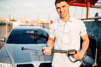 Man with high pressure washer on car wash station. Hand carwashing