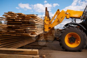Forklift loads the boards in the lumber yard outdoor. Autoloader works on timber mill warehouse, woodworking industry, carpentry. Wood processing on factory, forest sawing, sawmill