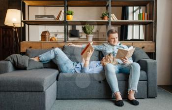 Young love couple resting on comfortable couch at home. Husband and wife relax in living room. Happy family together, man and woman reading books on sofa