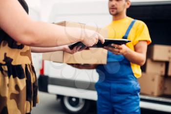 Cargo delivery service, male courier in uniform gives a parcel to the client, distribution business. Truck with cardboard parcels. Empty container