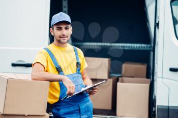 Workman or courier in uniform holds carton box in hands, truck with parcels on background. Distribution business. Cargo delivery. Empty, clear container