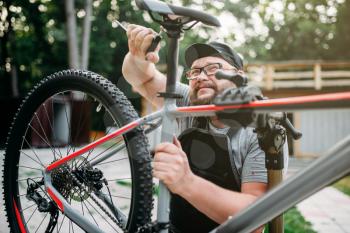 Bicycle mechanic adjusts with service tools bike seat. Cycle workshop outdoor. Bicycling sport, repairman at work