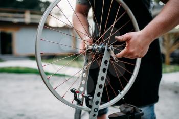 Male person in apron adjusts bike spokes and wheel with service tools. Cycle workshop outdoor. Bicycling sport, professional bicycle mechanic 