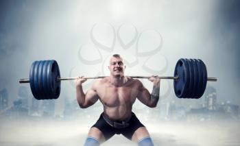 Muscular male weightlifter exercise with barbell, dark cityscape on background