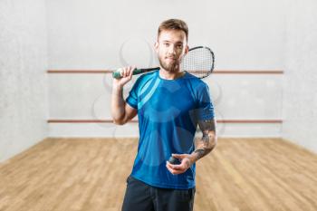 Squash game male player with racket and ball in hands, indoor training court on background