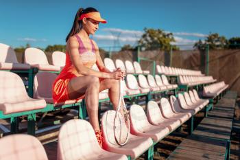 Young woman with tennis racket sitting on the podium. Summer season sport game. Active lifestyle