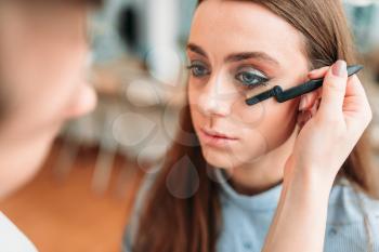 Makeup artist with brush in hand work with woman eyelashes, beauty studio on background. Cosmetic salon