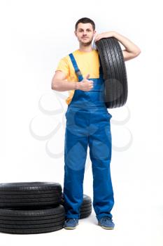 Serviceman in blue uniform holds tire in hand, white background, repairman with tyres