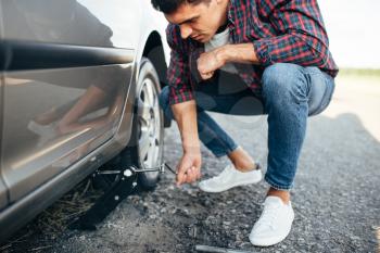 Man jack up broken car, wheel replacement. Vehicle with puncture tire on roadside
