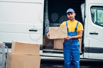 Workman or courier in uniform holds carton box in hands, truck with parcels on background. Distribution business. Cargo delivery. Empty, clear container