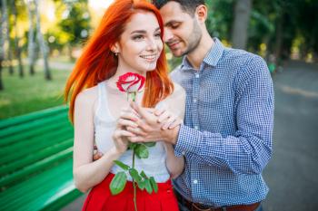 Love couple walk and hugs in summer park. Attracrive woman with rose and young man leisure together outdoors. Romantic date