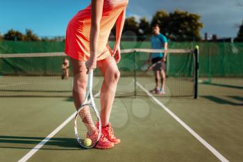 Young couple with tennis rackets plays on outdoor court. Summer season active sport game