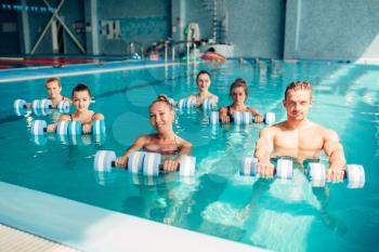 Women aqua aerobics traninig with dumbbells in indoor swimming pool. Female group with male trainer, water sport