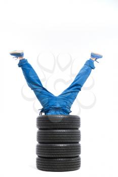 Tyre service, legs of the worker stick out of the pile of tires, white background, repairman, wheel mounting