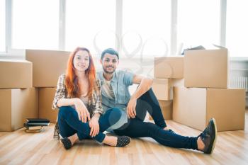 Happy couple sitting on the floor among cardboard boxes, moving to new house, housewarming