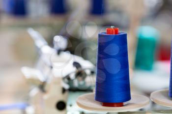 Spools of blue threads on sewing machine closeup. Cloth factory, weaving, textile production, clothing industry