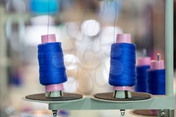 Spools of blue threads on sewing machine closeup. Cloth factory, weaving, textile production, clothing industry