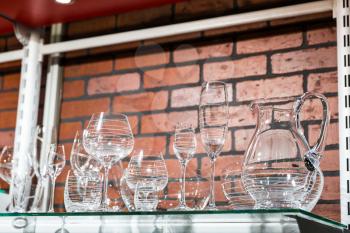 Transparent glass utensil on metal shelf, red brick background. Kitchenware shop