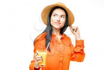 Happy woman in orange shirt and straw hat drinks freshly squeezedjuice, white background. Young girl with yellow beverage, healthy lifestyle