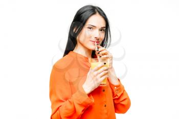 Cheerful woman in shirt and straw hat drinks freshly squeezed orange juice, white background. Young girl with yellow vitamin beverage, healthy lifestyle