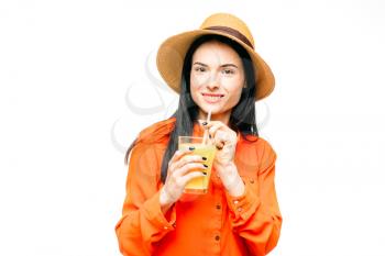 Happy woman in orange shirt and straw hat drinks freshly squeezed
juice, white background. Young girl with yellow beverage, healthy lifestyle