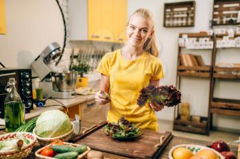 Happy woman holding salad on the kitchen, cooking healthy bio food. Vegetarian diet, fresh vegetables and fruits on wooden table