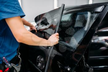 Male specialist applying car tinting film, installation process, tinted auto glass installing procedure