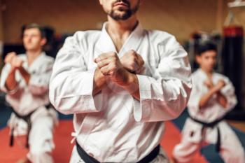 Martial arts karate fighters, master and his disciples in white kimono and black belts hone their skills, fight training in action, workout in gym