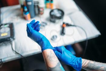 Female tattoo artist hands in blue sterile gloves, professional work tools on background. Tattooing in salon