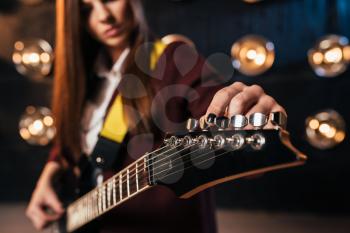 Female rock guitarist in suit tunes the guitar, stage with lights on background, retro style. Live music performer