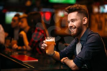 Young man drinks beer at the bar counter in a sport pub,