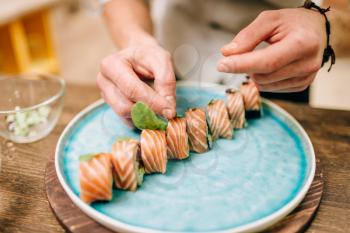 Male person cooking sushi rolls with salmon on wooden table, japanese food preparation process. Traditional asian cuisine, seafood delicious