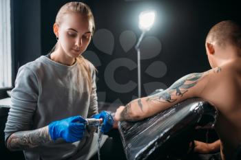 Female tattooist makes tattoo by machine on the shoulder. Professional tattooing in salon