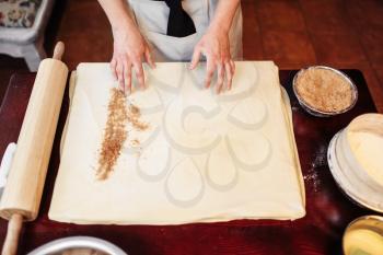 Male chef sprinkle the dough with cinnamon, apple strudel cooking. Homemade sweet dessert, tasty pie preparation process