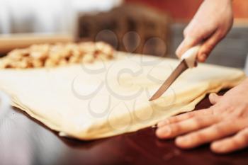 Male chef prepares apple strudel on wooden kitchen table, pastry ingredients on background. Homemade sweet dessert, pie preparation process
