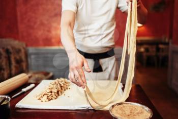 Male chef prepares dough for apple strudel on wooden kitchen table, pastry preparation process. Homemade sweet dessert